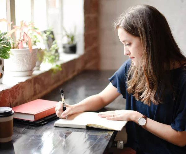 Wedding Budget - Woman Writing In A Notebook In Coffee Shop